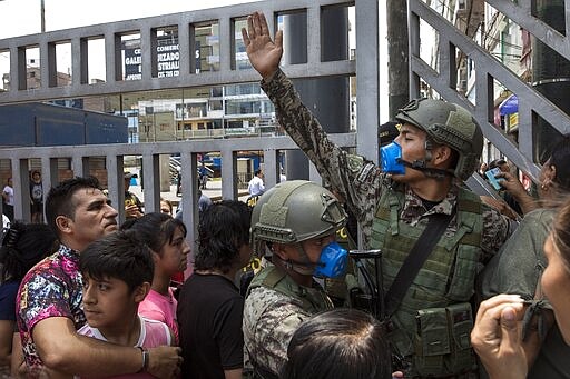 A soldier tries to organize people waiting to enter Gamarra clothing and textile market in Lima, Peru, Monday, March 16, 2020. Peruvian President Martin Vizcarra has declared a state of emergency, ordering citizens to stay in their homes and temporarily suspending certain constitutional rights, to contain the spread of coronavirus. According to the World Health Organization, most people recover in about two to six weeks from the new coronavirus, depending on the severity of the illness. (AP Photo/Rodrigo Abd)