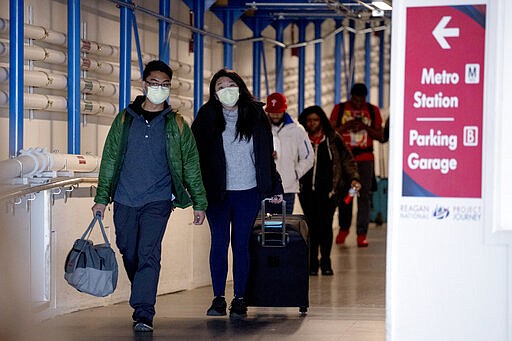 People wearing a masks walk through a terminal at Ronald Reagan Washington National Airport, Monday, March 16, 2020, in Arlington, Va. (AP Photo/Andrew Harnik)