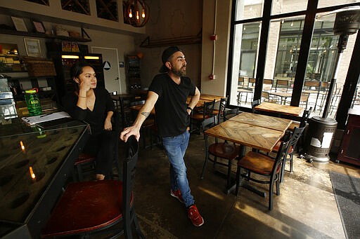 Server Diana Nguyen, left and manager Demetri Gregorakis stand in the empty dining room of The Rind, a wine, cheese and beer bar in Sacramento, Calif., Tuesday, March 17, 2020. The Rind, like other bars and restaurants, has seen a big drop in business since Gov. Gavin Newsom's guidelines restricting bars and restaurants amid the coronavirus outbreak. (AP Photo/Rich Pedroncelli)