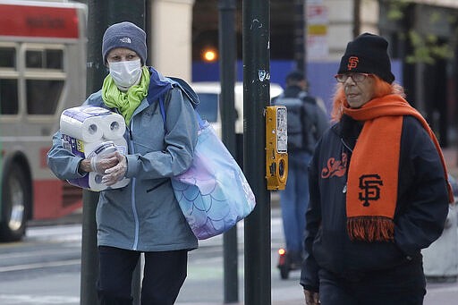 A woman wears a mask and gloves while carrying toilet paper across the street in San Francisco, Tuesday, March 17, 2020. Officials in seven San Francisco Bay Area counties have issued a shelter-in-place mandate affecting about 7 million people, including the city of San Francisco itself. The order says residents must stay inside and venture out only for necessities for three weeks starting Tuesday. (AP Photo/Jeff Chiu)