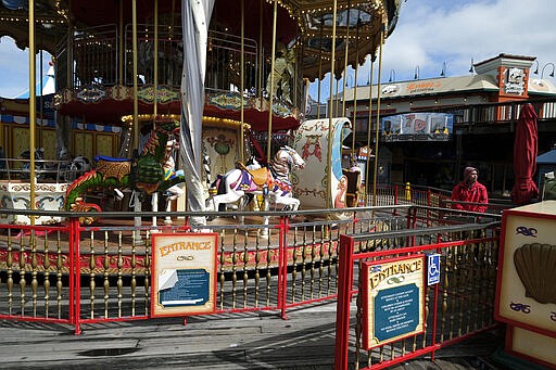 A Pier 39 carousel operator waits for riders at Fisherman's Wharf Monday, March 16, 2020, in San Francisco. Officials in six San Francisco Bay Area counties issued a shelter-in-place mandate Monday affecting nearly 7 million people, including the city of San Francisco itself. The order says residents must stay inside and venture out only for necessities for three weeks starting Tuesday in a desperate attempt by officials to curb the spread of the novel coronavirus. (AP Photo/Eric Risberg)