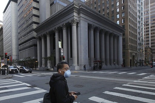 A man wearing a mask waits to cross an intersection in San Francisco, Tuesday, March 17, 2020. Officials in seven San Francisco Bay Area counties have issued a shelter-in-place mandate affecting about 7 million people, including the city of San Francisco itself. The order says residents must stay inside and venture out only for necessities for three weeks starting Tuesday. (AP Photo/Jeff Chiu)