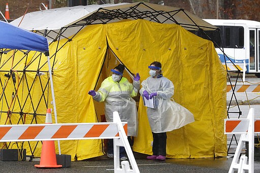 Medical personnel prepare for the arrival of a patient at a drive-through coronavirus testing facility at a site in a parking lot, at Cape Cod Community College, in Barnstable, Mass., Tuesday, March 17, 2020. For most people, the new coronavirus causes only mild or moderate symptoms, such as fever and cough. For some it can cause more severe illness. The vast majority of people recover from the virus. (AP Photo/Steven Senne)