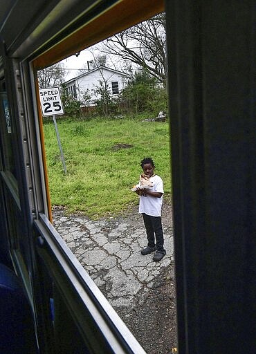 New Prospect Elementary School student Denario Cherry holds his meals after it was delivered along his bus route in Anderson, S.C., Tuesday morning, March 17, 2020. Anderson County School District 5 Culinary Services, with help from Principal Brian Williams and other staff helped deliver. (Ken Ruinard/The Independent-Mail via AP)