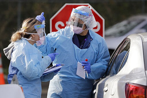 Theresa Malijan, a registered nurse, right, talks with medical assistant Miriam Fuentes as Malijan prepares to take a nasopharyngeal swab from a patient at a drive-through COVID-19 testing station for University of Washington Medicine patients Tuesday, March 17, 2020, in Seattle. The appointment-only drive-through clinic began a day earlier. Washington leads the country in the number of deaths, with most being associated with a nursing home in Kirkland. By Monday, the number of positive cases topped 900. (AP Photo/Elaine Thompson)