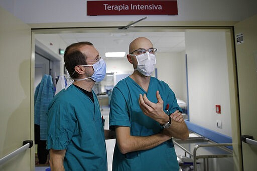 In this March 16, 2020, photo, Sergio Cattaneo, left, head of anesthesiology and intensive care of the Brescia Spedali Civili hospital, and ICU doctor Matteo Filippini talk with The Associated Press, in Brescia, Italy. Three weeks into Italy&#146;s coronavirus crisis, Cattaneo has seen an unused ward outfitted into an intensive care unit in six days, a hospital laundry room converted into a giant stretcher-filled waiting room and a tented field hospital erected outside to test possible new virus patients. (AP Photo/Luca Bruno)