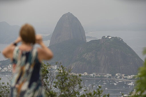 A tourist takes a picture of the Sugar Loaf mountain, in Rio de Janeiro, Brazil, Tuesday, March 17, 2020. The company that administers transport and installations at Rio's Sugarloaf Mountain, another postcard destination that sees 1.5 million visitors annually, said it is closing shop on Tuesday for 15 days as a measure to prevent the spread of the new coronavirus. (AP Photo/Silvia Izquierdo)