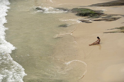 A woman sits on the sand at Arpoador beach in Rio de Janeiro, Brazil, Tuesday, March 17, 2020. Firemen began blaring recordings that urge beachgoers to stay home a a measure to prevent the spread of the new coronavirus, on Monday, one day before Rio's Gov. Wilson Witzel decreed a state of emergency. (AP Photo/Silvia Izquierdo)