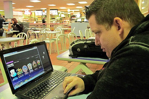 FILE - In this Nov. 21, 2013 file photo, Joseph Brennen of Ventnor N.J., logs on to a Harrah's online casino on his laptop from a highway rest area in Egg Harbor Township, N.J. on the first day of a test of Internet gambling in New Jersey. On Tuesday, March 17, 2020, many internet gambling providers said they've noticed a significant increase in business in the past week as many land-based casinos shut down due to the coronavirus. (AP Photo/Wayne Parry)