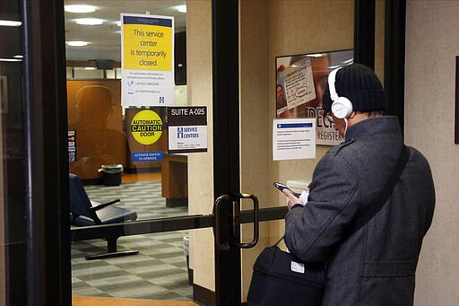 A man stands outside the locked doors of the Government Center service center Tuesday, March 17, 2020 in Minneapolis. Efforts to slow the spread of the coronavirus continu. across the state of Minnesota.  (AP Photo/Jim Mone)