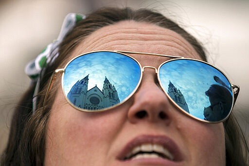 Kelly Seega of Massachusetts looks up to the twin spires of the Cathedral of St. John the Baptist, Tuesday, Mar., 17, 2020, in Savannah, Ga. The cathedral was closed to the public on an otherwise a very festive celebration of St. Patrick's Day. Last week, due to concerns about coronavirus, Savannah's mayor called off the city's 196-year-old parade. (AP Photo/Stephen B. Morton)