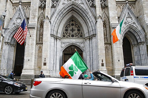 A woman holding an Irish themed flag is driven by St. Patrick's Cathedral after the annual parade was cancelled due to coronavirus concerns, Tuesday, March 17, 2020, in New York. New York state entered a new phase in the coronavirus pandemic Monday, as New York City closed its public schools, and officials said schools statewide would close by Wednesday. New York joined with Connecticut and New Jersey to close bars, restaurants and movie theaters along with setting limits on social gatherings. (AP Photo/John Minchillo)