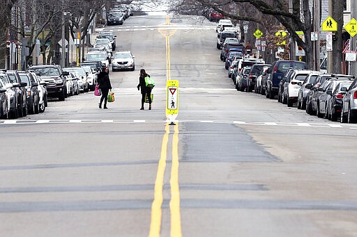 Two women walk with bags of groceries down a nearly empty Broadway on St. Patrick's Day in the South Boston neighborhood of Boston, Tuesday, March 17, 2020. For most people, the new coronavirus causes only mild or moderate symptoms. For some, it can cause more severe illness, especially in older adults and people with existing health problems. (AP Photo/Charles Krupa)