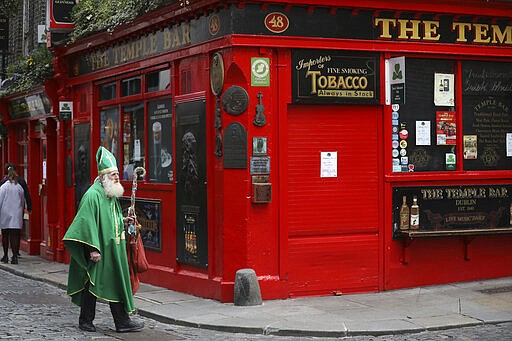 A man dressed as St Patrick walks past a closed Temple bar in Dublin city centre, Monday, March, 16, 2020. All pubs in the Republic of Ireland closed late Sunday to try and tackle the spread of Covid-19. For most people, the new coronavirus causes only mild or moderate symptoms. For some it can cause more severe illness, especially in older adults and people with existing health problems.(AP Photo/Peter Morrison)