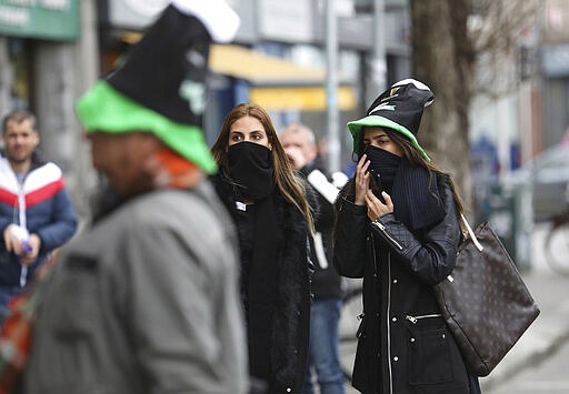 Tourists cover their faces in Dublin city centre, Tuesday March 17, 2020. The St Patrick's Day parades across Ireland were cancelled due to the outbreak of Covid-19 virus. For most people, the new COVID-19 coronavirus causes only mild or moderate symptoms, but for some it can cause more severe illness. (AP Photo/Peter Morrison)