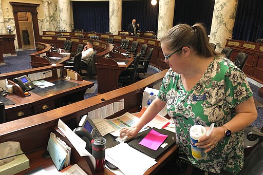 Joy Thomas, chief of staff for the minority Democratic party, wipes down desks in the Idaho House of Representatives at the Statehouse in Boise, Idaho, Tuesday, March 17, 2020. Two Idaho lawmakers are getting out of the Statehouse due to fears from the new coronavirus and others say their decision to remain is day to day. (AP Photo/Keith Ridler)