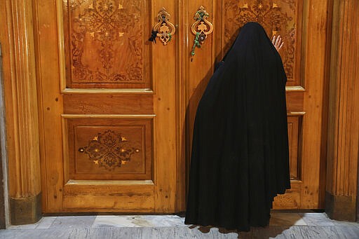 A woman prays behind a closed door of Masoume shrine in the city of Qom, some 80 miles (125 kilometers) south of the capital Tehran, Iran, Monday, March 16, 2020. On Monday, Iran closed the Masoume shrine, a major pilgrimage site in the city of Qom, the epicenter of the country's new coronavirus outbreak. Authorities were already restricting access and barring pilgrims from kissing or touching the shrine, but it had remained open. (AP Photo/Str)