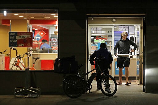 A man uses his elbow to open the door as he walks out of a Domino's Pizza restaurant in downtown Seattle as a delivery driver walks in, Sunday, March 15, 2020. Washington Gov. Jay Inslee said Sunday night that he would order all bars, restaurants, entertainment and recreation facilities in the state to temporarily close to fight the spread of the COVID-19 coronavirus. Inslee said that restaurants could continue take-out and delivery services. (AP Photo/Ted S. Warren)