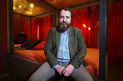 Aurel Johannes Marx sits on a bed in his three room brothel 'Lankwitzer 7' as he poses for photo after and interview with the Associated Press in Berlin, Germany, Friday, March 13, 2020. Sex for sale has long been a staple part of the German capital's hedonistic nightlife, but amid concerns over the new coronavirus even the world's supposedly oldest profession is being hit by a sudden slump. For some, especially older adults and people with existing health problems, it can cause more severe illness, including pneumonia. (AP Photo/Markus Schreiber)