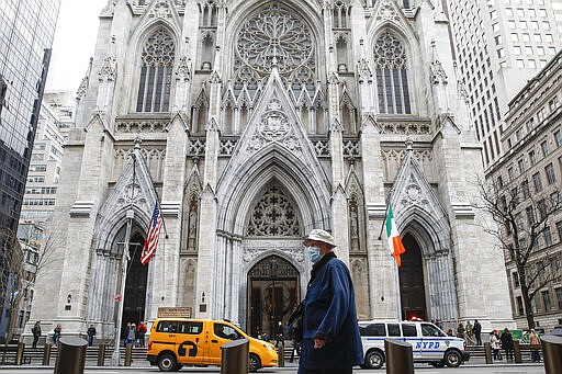 A pedestrian wearing a protective mask walks by St. Patrick's Cathedral after the annual St. Patrick's Day parade was cancelled due to coronavirus concerns, Tuesday, March 17, 2020, in New York. New York state entered a new phase in the coronavirus pandemic Monday, as New York City closed its public schools, and officials said schools statewide would close by Wednesday. New York joined with Connecticut and New Jersey to close bars, restaurants and movie theaters along with setting limits on social gatherings. (AP Photo/John Minchillo)