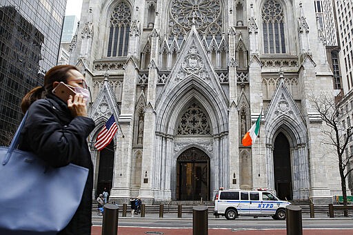 A pedestrian wearing a protective mask walks by St. Patrick's Cathedral after the annual St. Patrick's Day parade was cancelled due to coronavirus concerns, Tuesday, March 17, 2020, in New York. New York state entered a new phase in the coronavirus pandemic Monday, as New York City closed its public schools, and officials said schools statewide would close by Wednesday. New York joined with Connecticut and New Jersey to close bars, restaurants and movie theaters along with setting limits on social gatherings. (AP Photo/John Minchillo)