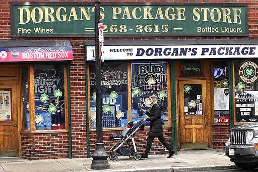 A woman pushes a stroller past a liquor store on a nearly empty sidewalk on Broadway on St. Patrick's Day in the South Boston neighborhood of Boston, Tuesday, March 17, 2020. For most people, the new coronavirus causes only mild or moderate symptoms. For some, it can cause more severe illness, especially in older adults and people with existing health problems. (AP Photo/Charles Krupa)