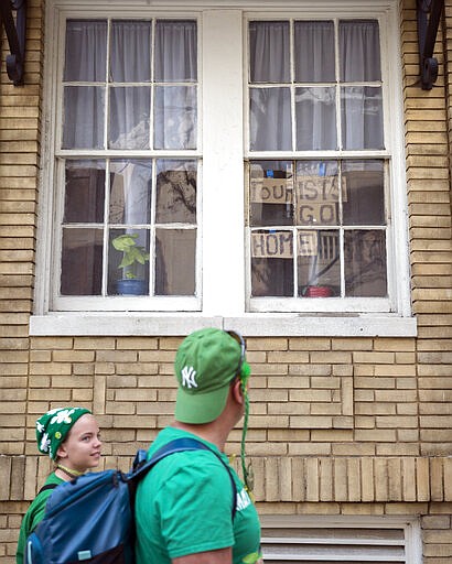 A family dressed in St. Patrick's Day attire walks past a window with a message for tourist, Tuesday, March, 17, 2020, in downtown Savannah, Ga. Due to concerns about coronavirus Savannah's mayor called off the city's 196-year-old St. Patrick's Day parade. (AP Photo/Stephen B. Morton)