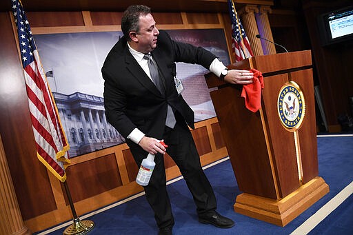 Mike Mastrian, director of the Senate Radio and Television Gallery, cleans down the podium before a news conference with Senate Minority Leader Sen. Chuck Schumer of N.Y., on Capitol Hill in Washington, Tuesday, March 17, 2020. (AP Photo/Susan Walsh)