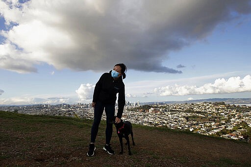 Lisa Wang wears a mask while walking her dog Rooney on Bernal Heights Hill in San Francisco, Monday, March 16, 2020. Officials in six San Francisco Bay Area counties issued a shelter-in-place mandate Monday affecting nearly 7 million people, including the city of San Francisco itself. The order says residents must stay inside and venture out only for necessities for three weeks starting Tuesday in a desperate attempt by officials to curb the spread of the novel coronavirus. (AP Photo/Jeff Chiu)