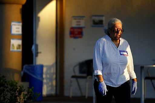 A polling place worker uses gloves outside of the Boca Raton Library during the Florida primary election, Tuesday, March 17, 2020, in Boca Raton, Fla.  As Florida officials try to contain the spread of the novel coronavirus, the state's voters headed to the polls to cast ballots in the Democratic presidential primary.  (AP Photo/Julio Cortez)