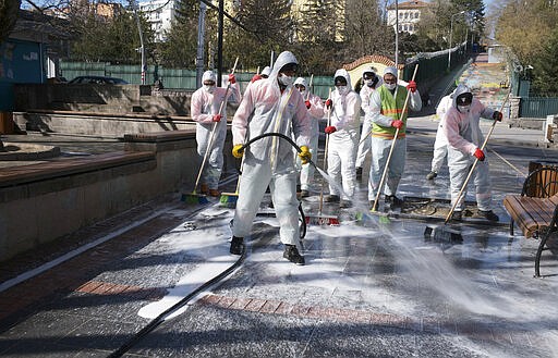 Municipality workers wearing face masks and protective suits disinfect Kugulu public garden amid the coronavirus outbreak, in Ankara, Turkey, Tuesday, March 17, 2020. For most people, the new coronavirus causes only mild or moderate symptoms. For some it can cause more severe illness. (AP Photo/Burhan Ozbilici)