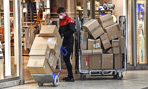 A parcel carrier with a face mask brings packages to a shop in Cologne, Germany, Tuesday, March 17, 2020. The city closed all bars and restaurants due to the coronavirus outbreak, all shops except supermarkets are also expected close. All public and private events are banned. For most people, the new coronavirus causes only mild or moderate symptoms, such as fever and cough. For some, especially older adults and people with existing health problems, it can cause more severe illness, including pneumonia. (AP Photo/Martin Meissner)