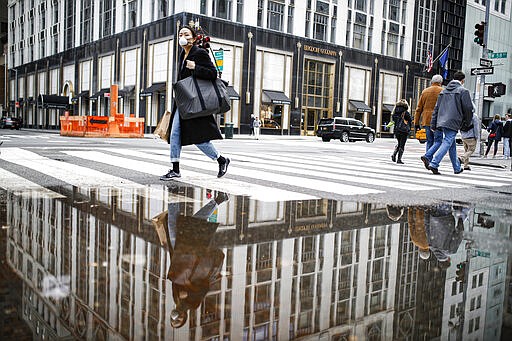 A pedestrian wearing a protective face mask is reflected in a rain puddle, Tuesday, March 17, 2020, in New York. New York state entered a new phase in the coronavirus pandemic this week, as New York City closed its public schools, and officials said schools statewide would close by Wednesday. New York joined with Connecticut and New Jersey to close bars, restaurants and movie theaters along with setting limits on social gatherings. (AP Photo/John Minchillo)