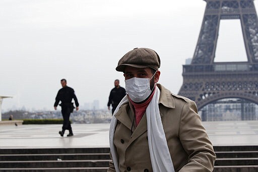 A masked man walks on the empty Trocadero as Police officers patrol in background, next to the Eiffel Tower, in Paris, Tuesday, March 17, 2020. French President Emmanuel Macron said that starting on Tuesday, people would be allowed to leave the place they live only for necessary activities such as shopping for food, going to work or taking a walk. For most people, the new coronavirus causes only mild or moderate symptoms. For some it can cause more severe illness. (AP Photo/Francois Mori)