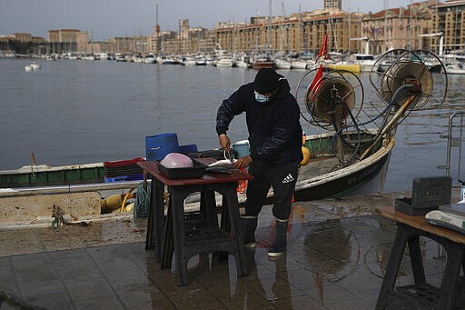 A masked fisherman works Tuesday, March 17, 2020 on the port of Marseille, southern France. French President Emmanuel Macron announced strong restrictions on freedom of movement in a bid to counter the new coronavirus, as the European Union closed its external borders to foreign travelers. For most people, the new coronavirus causes only mild or moderate symptoms. For some it can cause more severe illness. (AP Photo/Daniel Cole)