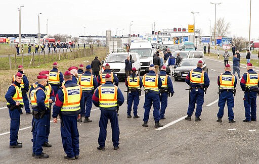 Police officers block the road at the Austrian border in Hegyeshalom, northwestern Hungary, Tuesday, March 17, 2020. By noon an almost 20-kilometer long line of cars waited on the Austrian side of the border. The Romanian Minister of Foreign Affairs has requested that Hungary open a humanitarian corridor for the Romanian citizens stuck in Hegyeshalom. Due to the coronavirus pandemic as of this day only Hungarian citizens can enter the country. Freight traffic continues as usual. For most people, the new coronavirus causes only mild or moderate symptoms, such as fever and cough. For some, especially older adults and people with existing health problems, it can cause more severe illness, including pneumonia.(Csaba Krizsan/MTI via AP)