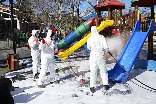 Municipality workers wearing face masks and protective suits disinfect Kugulu public garden amid the coronavirus outbreak, in Ankara, Turkey, Tuesday, March 17, 2020. For most people, the new coronavirus causes only mild or moderate symptoms. For some it can cause more severe illness. (AP Photo/Burhan Ozbilici)