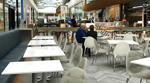 A couple sit alone at a coffee shop area at a shopping centre in London, Tuesday, March 17, 2020. For most people, the new coronavirus causes only mild or moderate symptoms, such as fever and cough. For some, especially older adults and people with existing health problems, it can cause more severe illness, including pneumonia. (AP Photo/Kirsty Wigglesworth)