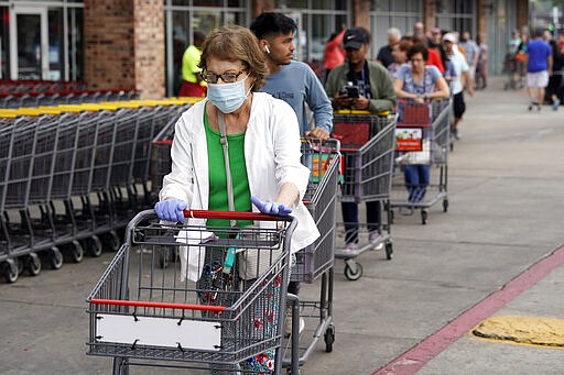 Ruth Flavelle wears a mask and gloves as she enters an H-E-B grocery after waiting in line with more than 150 people Tuesday, March 17, 2020, in Spring, Texas.  Grocery store executives and city officials reassured the community, on Monday, that plenty of food will be available in their stores and urged people not to stockpile groceries amid coronavirus concerns. (AP Photo/David J. Phillip)