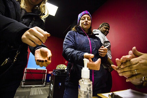 Sharon Trask and other voters use hand sanitizer as they stand in line to vote at Lincoln Lodge Polling station, 1st ward, Tuesday, March 17  2020 in Chicago.  Voters across the state are getting the chance to decide competitive primary races for the U.S. House and the Illinois Supreme Court, with concerns about the coronavirus looming large. Election officials have been promoting voting early and casting ballots by mail in an attempt to control crowds and curb the spread. The vast majority of people recover from the new coronavirus. According to the World  Health Organization, most people recover in about two to six weeks, depending on the severity of the illness. (James Foster/Chicago Sun-Times via AP)