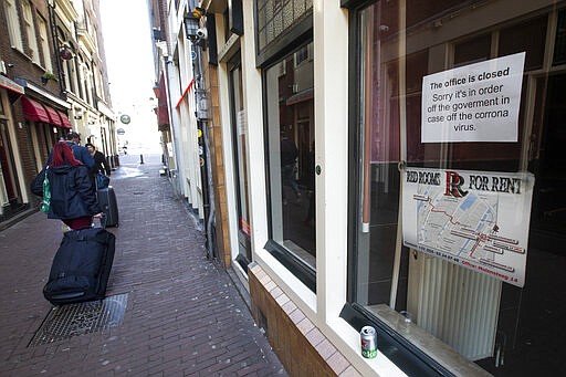 Two tourists pull their suitcases passing closed windows of sex workers in the Red Light District of Amsterdam, Netherlands, Monday, March 16, 2020. Health minister Bruno Bruins ordered all Dutch schools, cafes, restaurants coffeeshops, saunas, sex clubs and sport and fitness clubs to be closed from Sunday March 15th onwards as the government sought to prevent the further spread of coronavirus in the Netherlands. For most people, the new coronavirus causes only mild or moderate symptoms, such as fever and cough. For some, especially older adults and people with existing health problems, it can cause more severe illness, including pneumonia. (AP Photo/Peter Dejong)