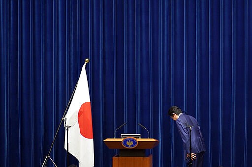 FILE - In this March 14, 2020, file photo, Japanese Prime Minister Shinzo Abe bows to toward a Japanese flag before delivering his speech at the Prime Minister's office in Tokyo. Prime Minister Abe might be the biggest loser if the Tokyo Olympics don't go off as planned in just over four months. Abe has attached himself to the success of the Olympics since pushing hard for Tokyo's selection at an IOC meeting in 2013 in Buenos Aires, Argentina. Tokyo was picked over Istanbul by billing itself as a &#147;safe pair of hands.&quot;  (AP Photo/Eugene Hoshiko, File)