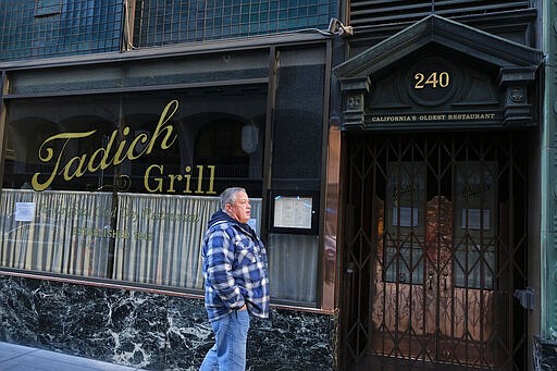 A man stands in front of the shuttered Tadich Grill in the Financial District and looks down California Street Monday, March 16, 2020, in San Francisco. Officials in seven San Francisco Bay Area counties have issued a shelter-in-place mandate affecting about 7 million people, including the city of San Francisco itself. The order says residents must stay inside and venture out only for necessities for three weeks starting Tuesday. It's the latest effort by officials to curb the spread of the novel coronavirus. The restaurant is California's oldest continually running restaurant dating to 1849. (AP Photo/Eric Risberg)