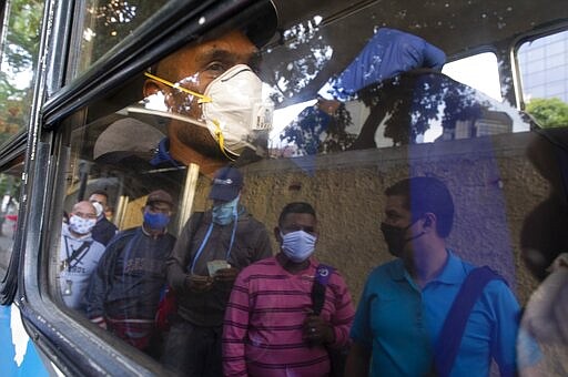 People wearing protective masks as a precaution against the spread of the new coronavirus are reflected on a bus window, in Caracas, Venezuela, Tuesday, March 17, 2020. President Nicolas Maduro ordered citizens to stay home, and to wear a mask when in public. The vast majority of people recover from the new virus. (AP Photo/Ariana Cubillos)