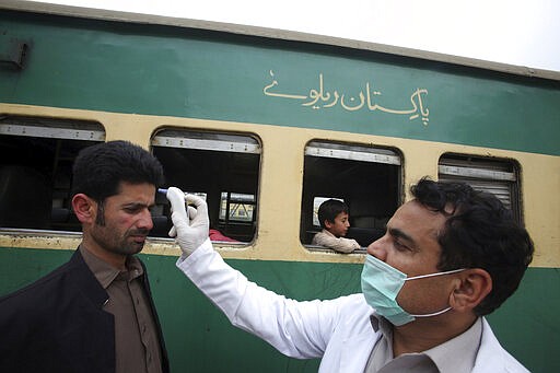 A Pakistani volunteer checks the body temperature of passengers arriving at a railway station in Peshawar, Pakistan, Tuesday, March 17, 2020. For most people, the new coronavirus causes only mild or moderate symptoms. For some it can cause more severe illness. (AP Photo/Muhammad Sajjad)