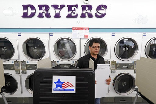 Guillermo Cruz-Sanchez takes his ballot to the ballot box at the Su Nueva Lavanderia polling place Tuesday, March 17, 2020, in Chicago.   Voters across the state are getting the chance to decide competitive primary races for the U.S. House and the Illinois Supreme Court, with concerns about the coronavirus looming large. (AP Photo/Charles Rex Arbogast)