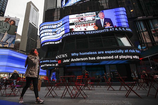 FILE - In this Wednesday, March 11, 2020, file photom pedestrians pass under a news ticker showing news about the new coronavirus outbreak in Times Square, in New York. Factories in China, struggling to reopen after the coronavirus shut down the economy, face a new threat from U.S. anti-disease controls that might disrupt the flow of microchips and other components they need. For most people, the new coronavirus causes only mild or moderate symptoms. For some it can cause more severe illness. (AP Photo/John Minchillo, File)