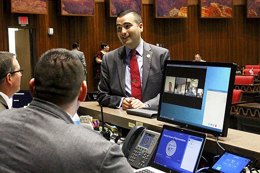 Republican Rep. T.J. Shope speaks with Arizona House clerks as members who are being allowed to vote remotely because of coronavirus concerns appear on a computer screen before a floor session at the Capitol in Phoenix , Wednesday, March 18, 2020. The House hopes to quickly pass a bare-bones budget and send it to the Senate before adjourning until the coronavirus crisis ebbs. (AP Photo/Bob Christie)