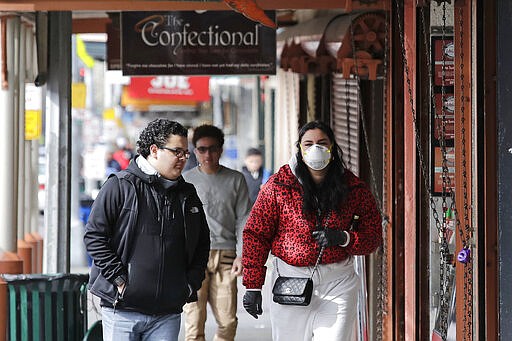 Pedestrians walk past some closed shops at Pike Place Market on Tuesday, March 17, 2020, in Seattle. Many shops in the landmark market continue to remain open, though business has dropped considerably in recent weeks. A day earlier, Washington Gov. Jay Inslee ordered all bars, restaurants, entertainment and recreation facilities to temporarily close to fight the spread of COVID-19 in the state with by far the most deaths in the from the disease. (AP Photo/Elaine Thompson)