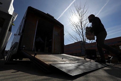 In this Tuesday, March 17, 2020, a worker loads food onto a trailer for delivery at the Des Moines Area Religious Council food pantry in Des Moines, Iowa.  With the new coronavirus leaving many people at least temporarily out of work, food banks and pantries across the U.S. are scrambling to meet an expected surge in demand, even as older volunteers have been told to stay home and calls for social distancing have complicated efforts to package and distribute food. (AP Photo/Charlie Neibergall)